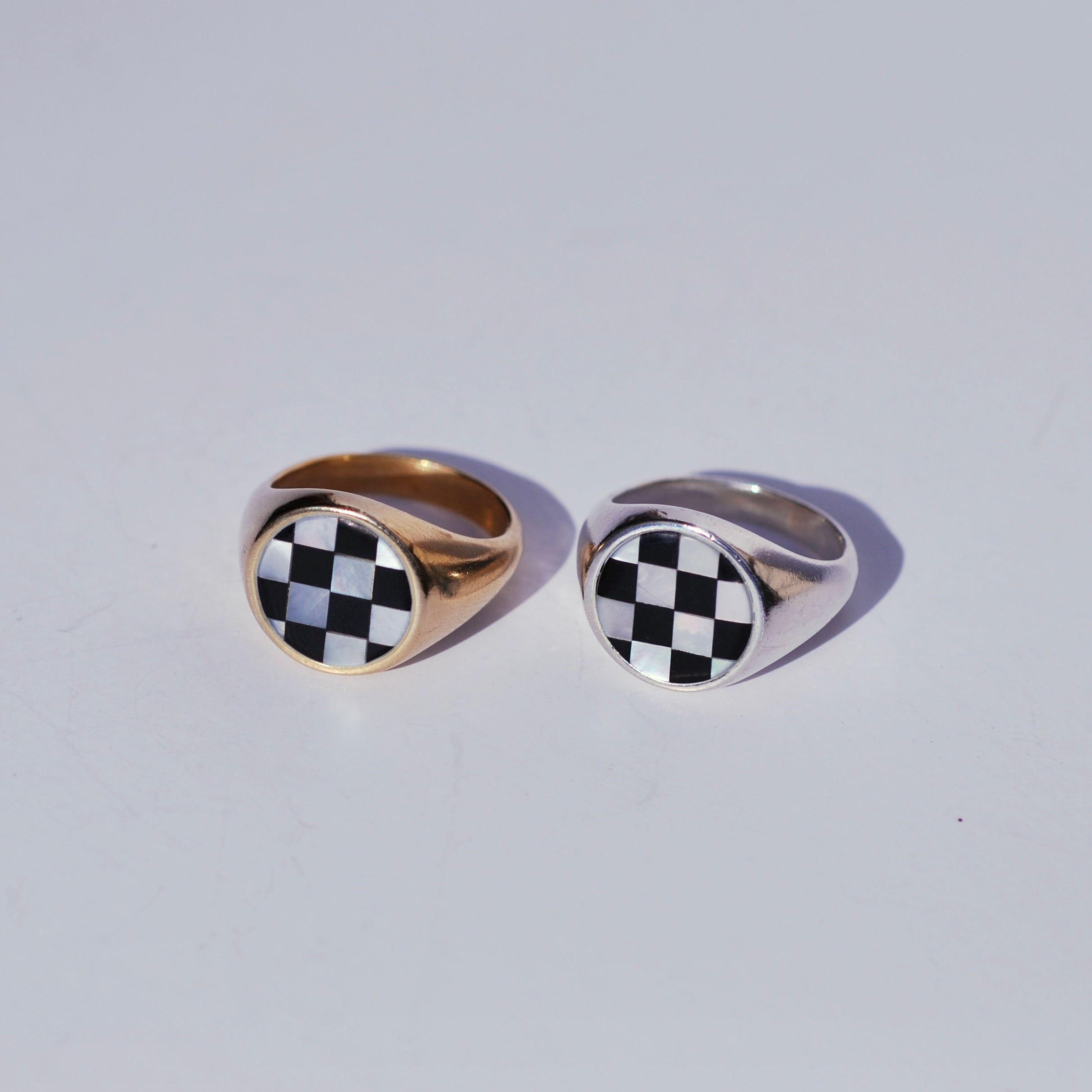 Two round signets with large checkerboard inlay faces, one bronze and one silver on a white background