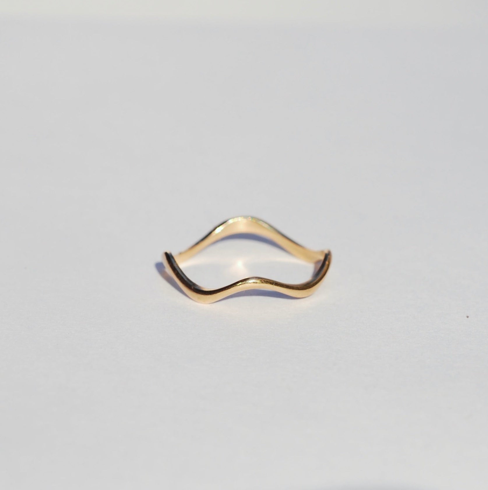 Thin wavy gold ring on a grey background