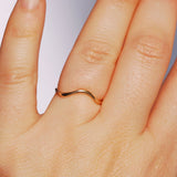 Hand wearing a wavy gold ring on a plain background