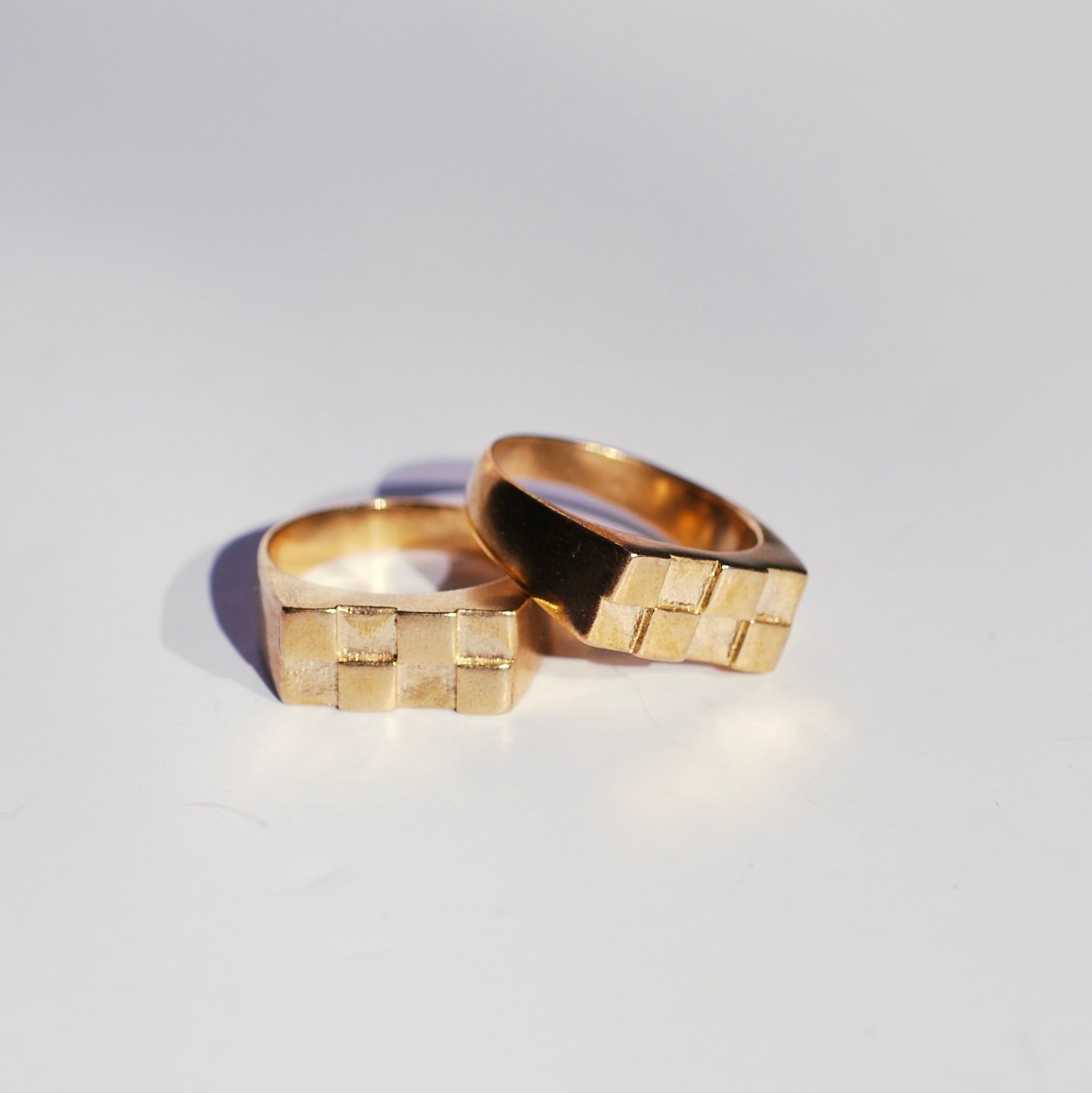 Two bronze signet rings with rectangular faces and a checkerboard pattern on a white background