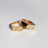 Two bronze signet rings with rectangular faces and a checkerboard pattern on a white background