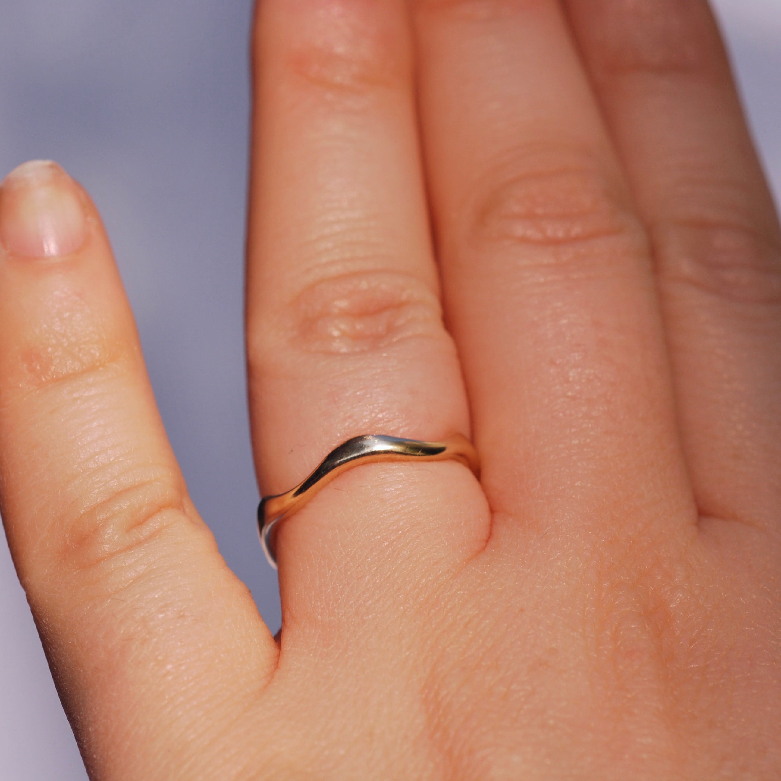 Close-up of a hand wearing a gold ring with a blurred background