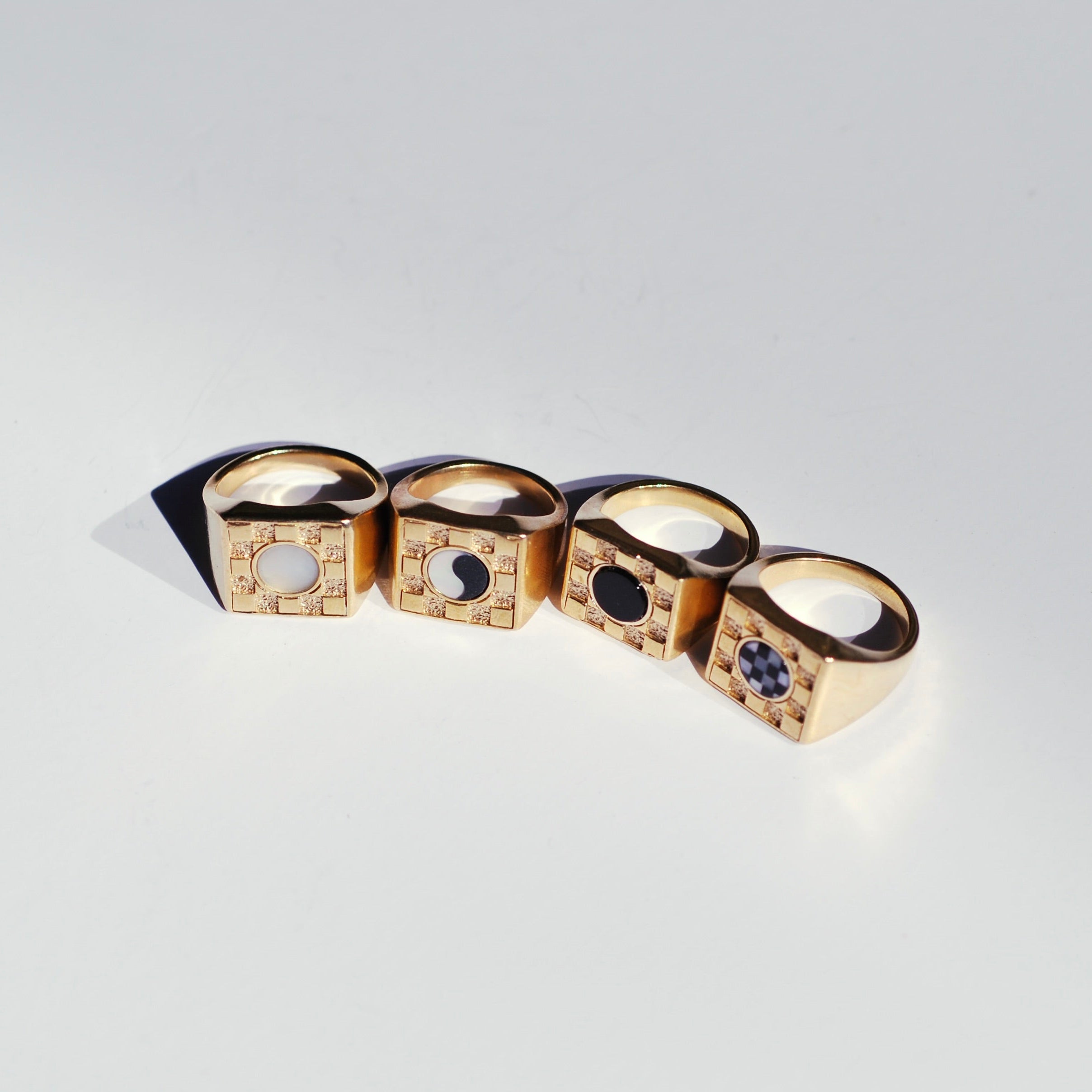 Four bronze square checkerboard signets with different color stone options on a white background