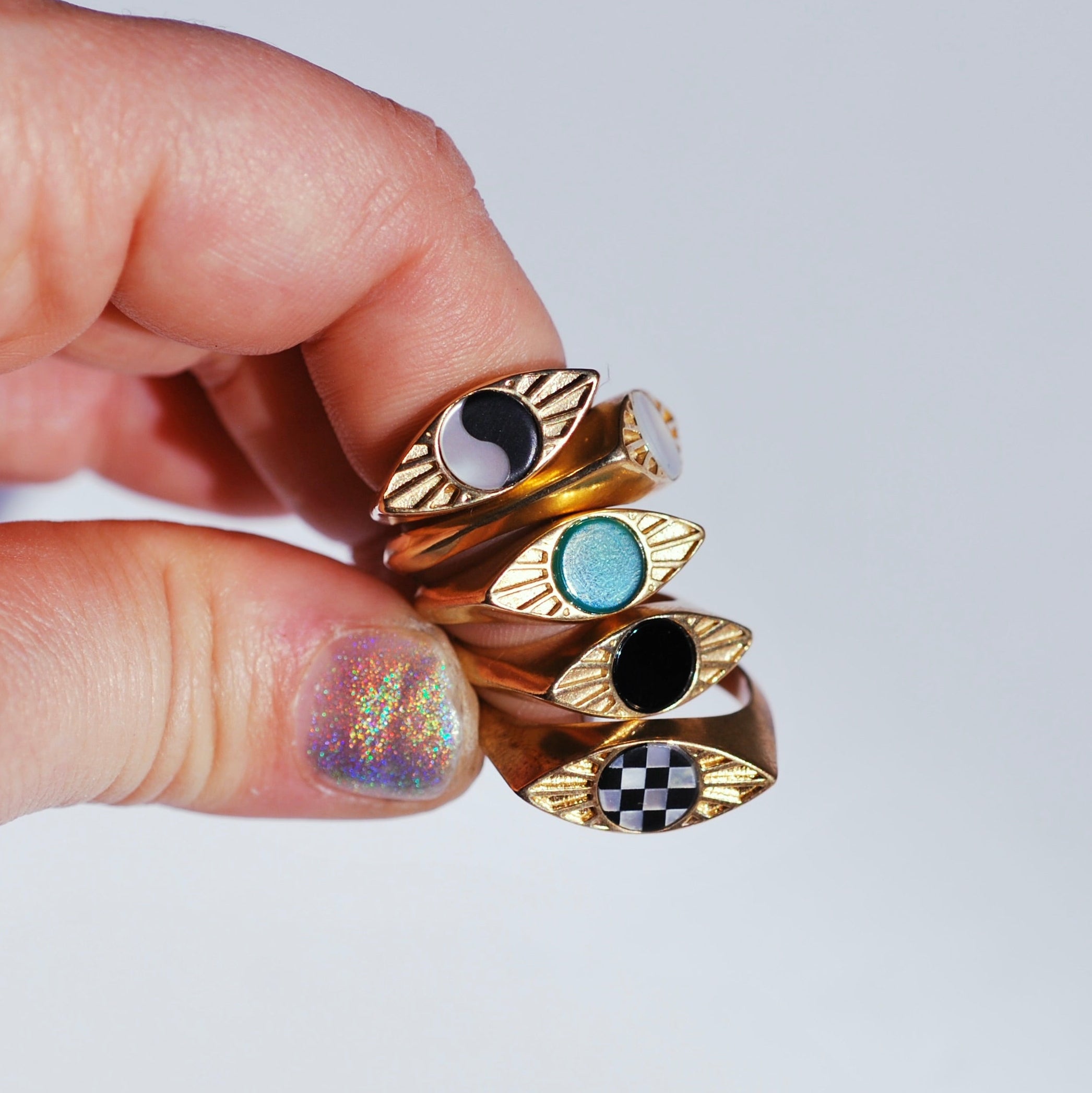 Hand holding five bronze stacked eye shaped signets with different round inlay stones in the center