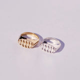 Two bronze and silver oval signet rings with a diamond pattern on their faces, on a light gray background
