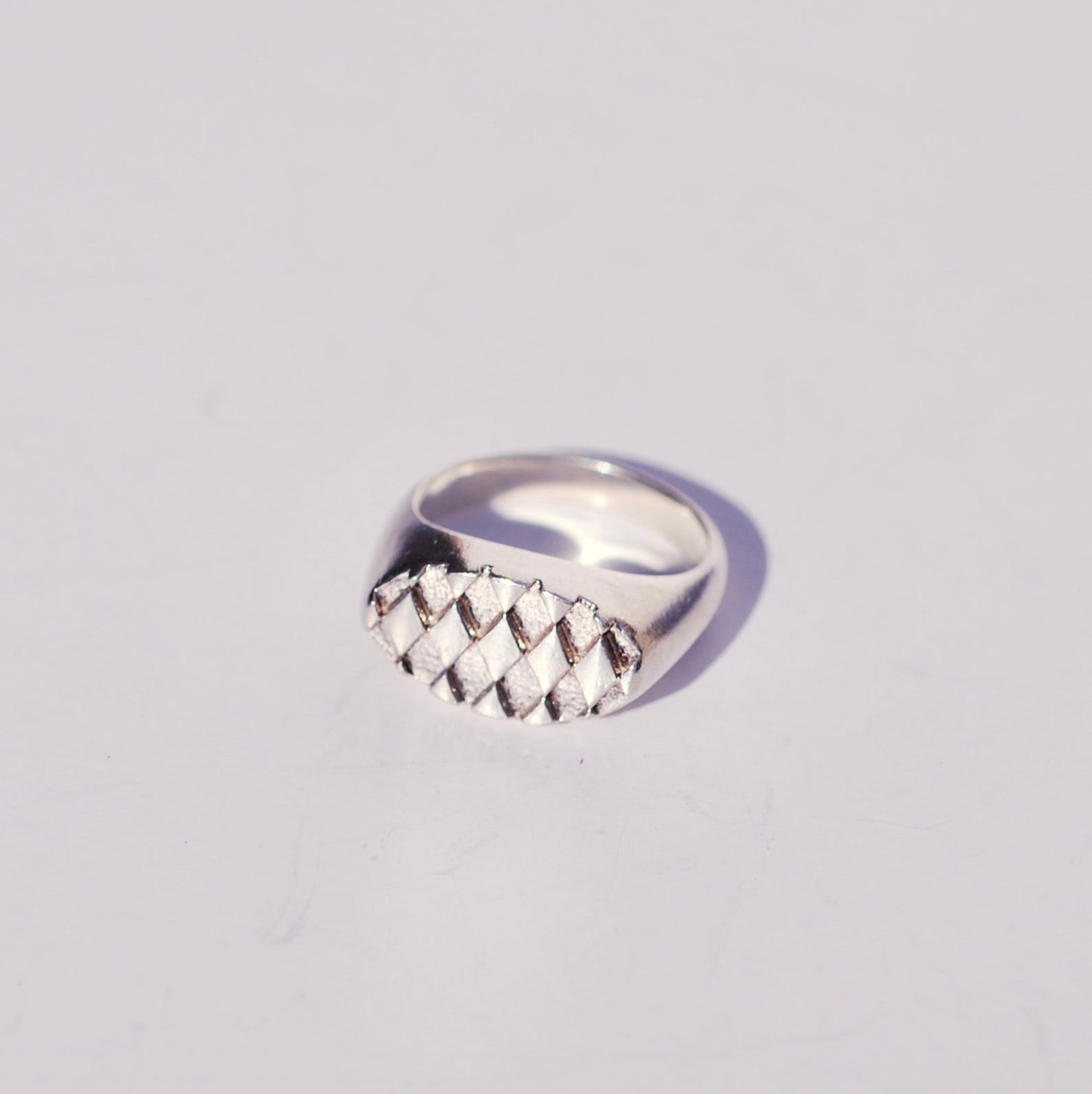 Silver oval signet  ring with a diamond textured face on a light gray background
