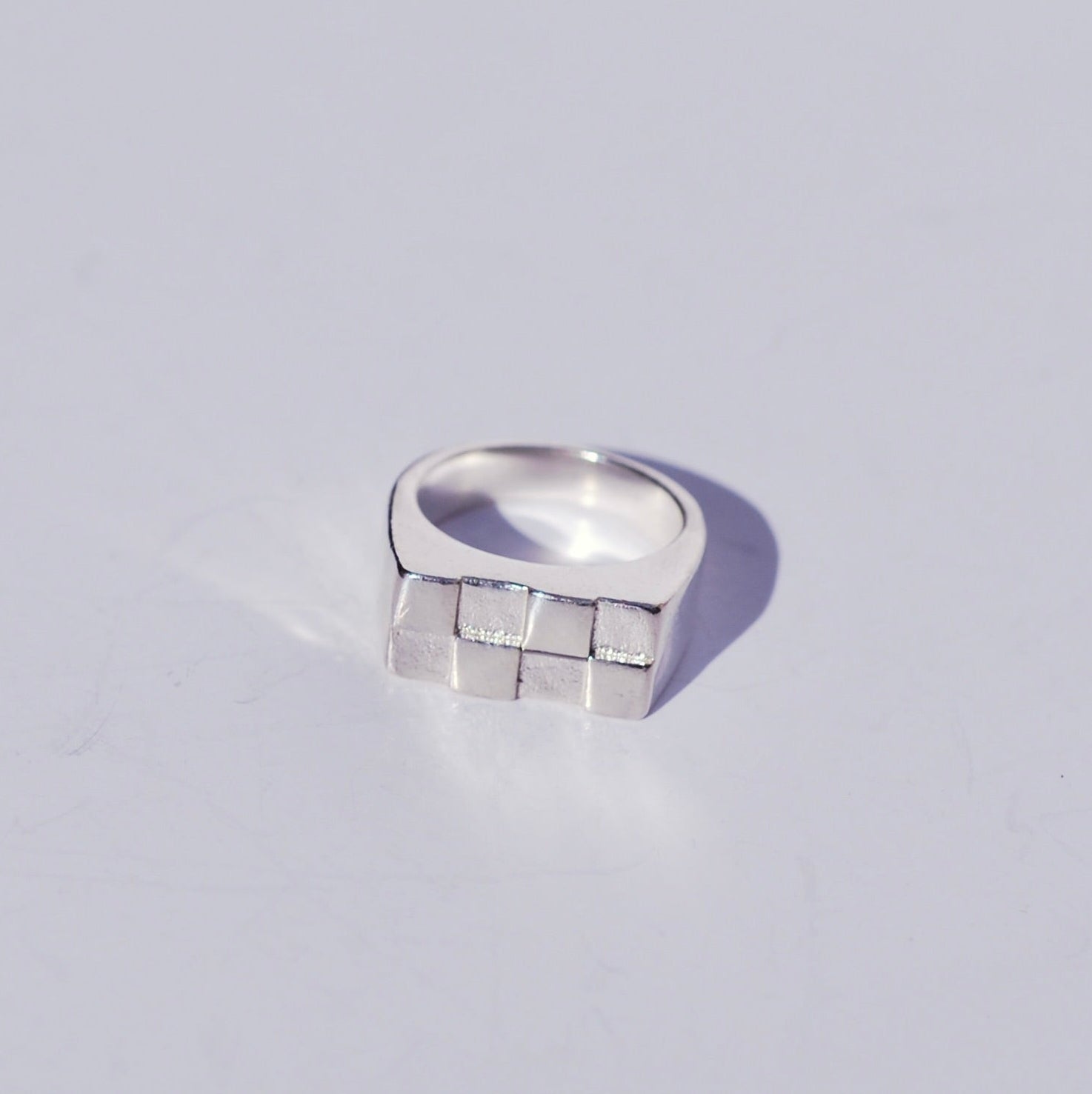 Silver rectangle signet ring with a checkerboard geometric design on a light gray background