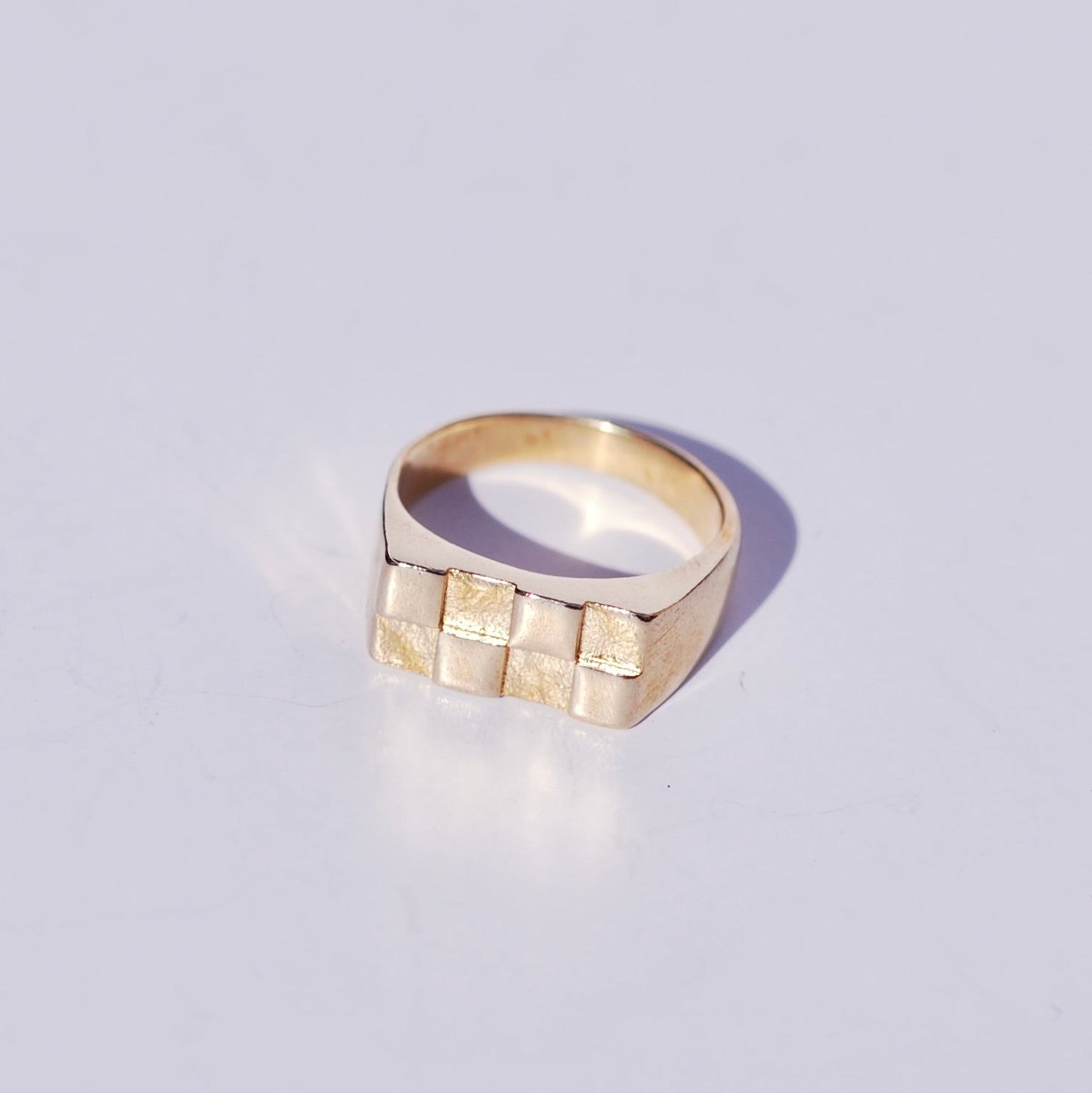Gold signet ring with a checkered pattern on a light gray background