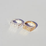 Two rectangular signet rings, one silver and one bronze with checkerboard faces, on a light gray background