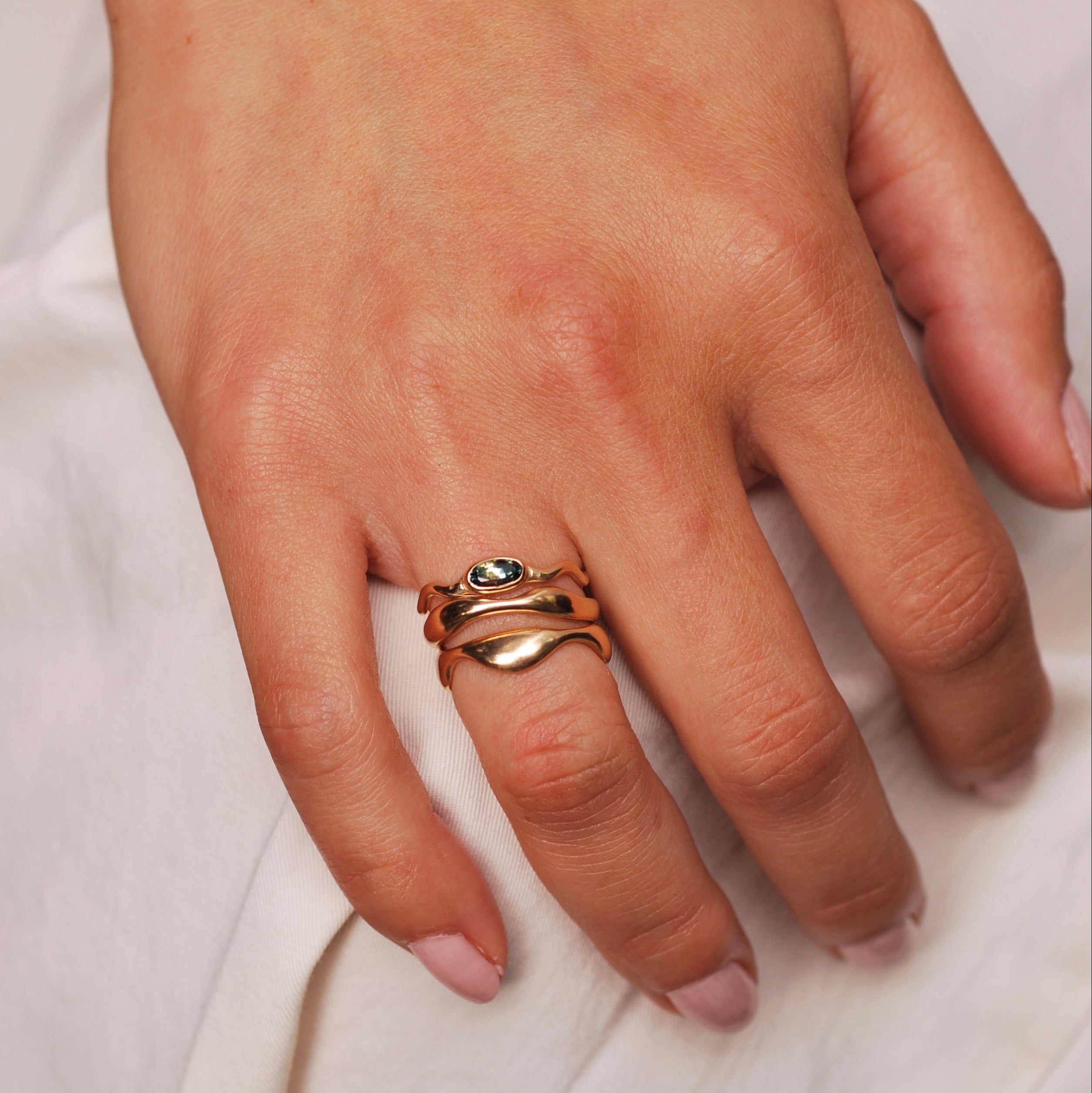 Hand wearing a gold ring stack of wavy organic stacking bands on a light background