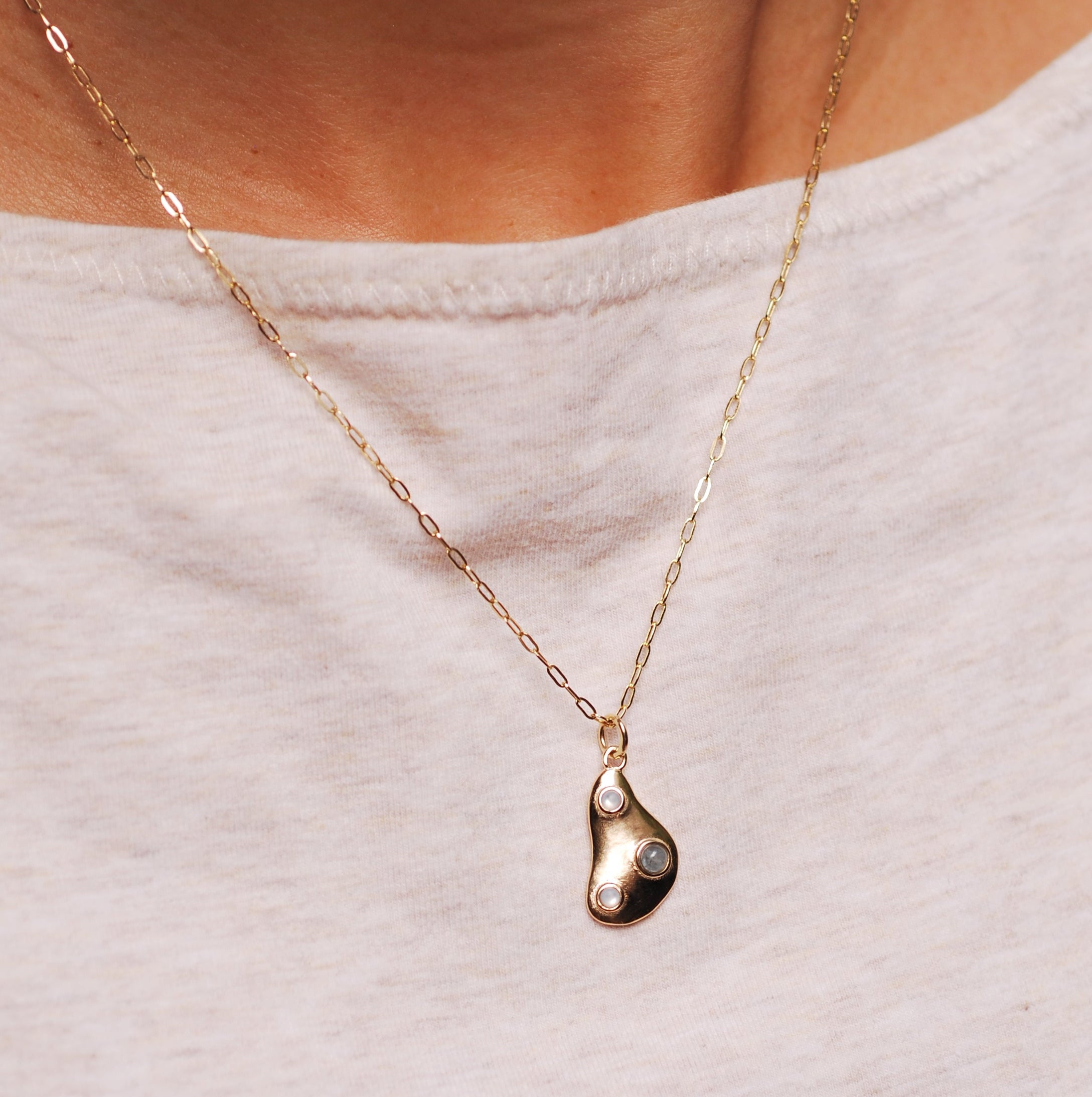 Gold necklace with a teardrop pendant and 3 stones on a light grey background