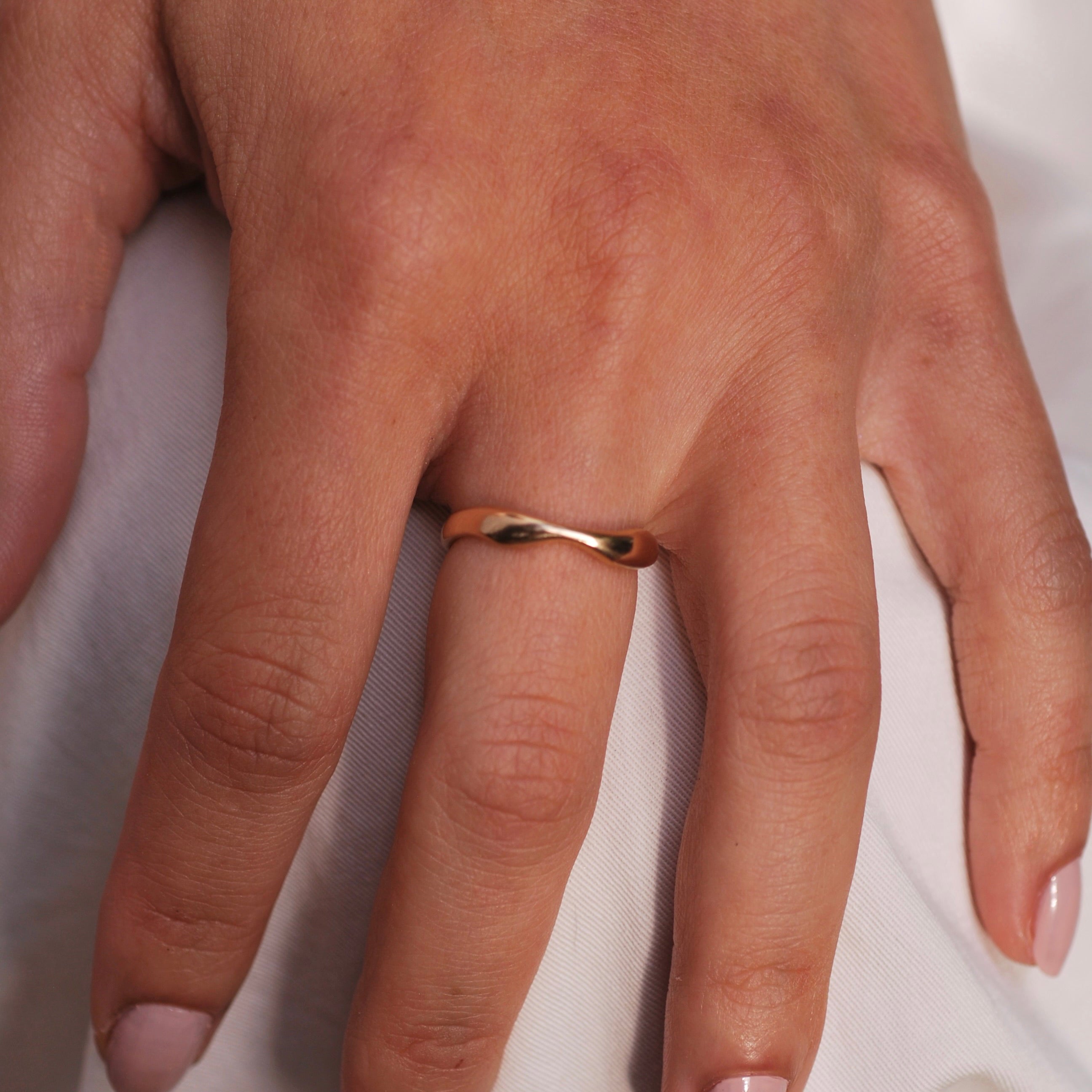 Hand wearing a gold ring on a light background