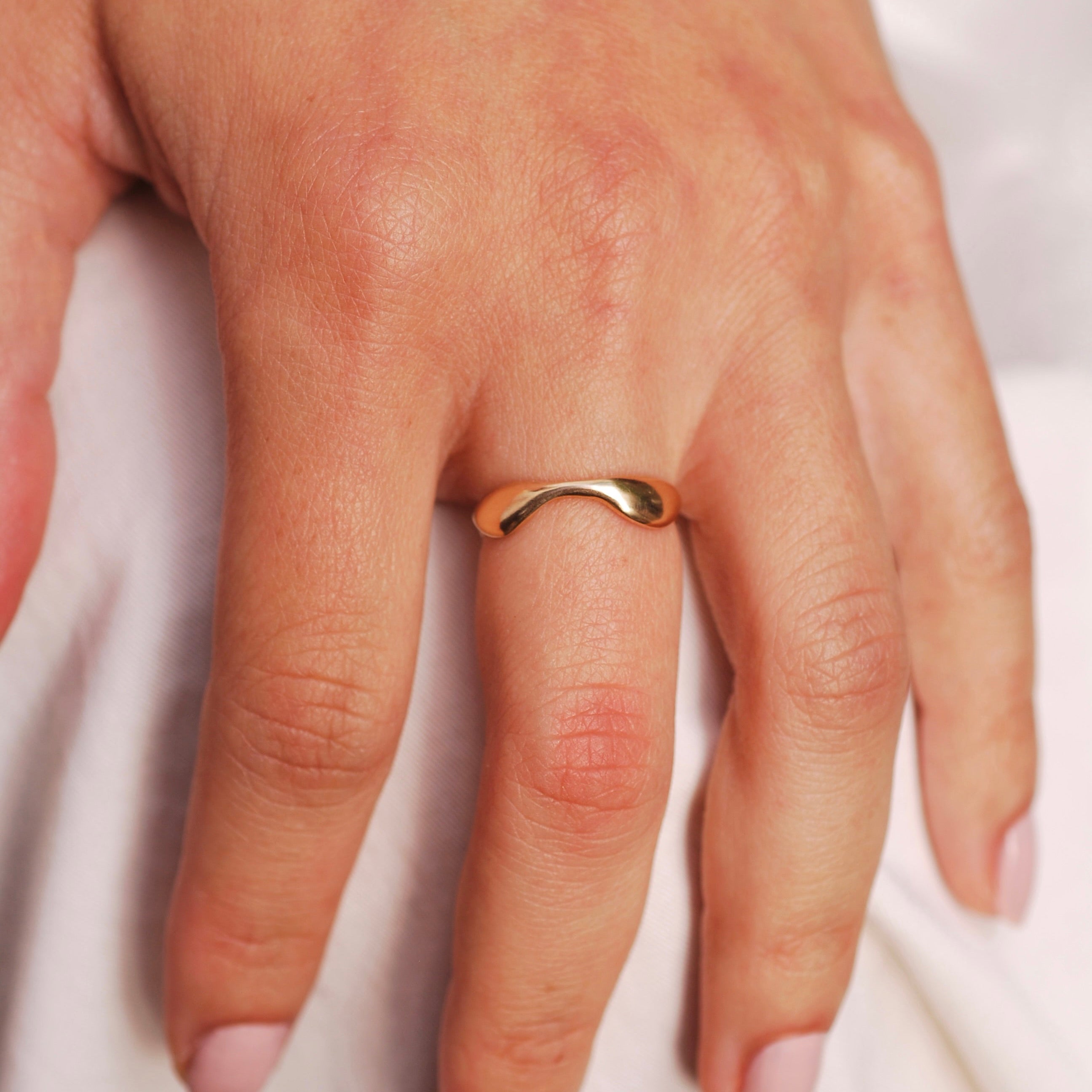 Hand wearing a gold scalloped ring on a white background