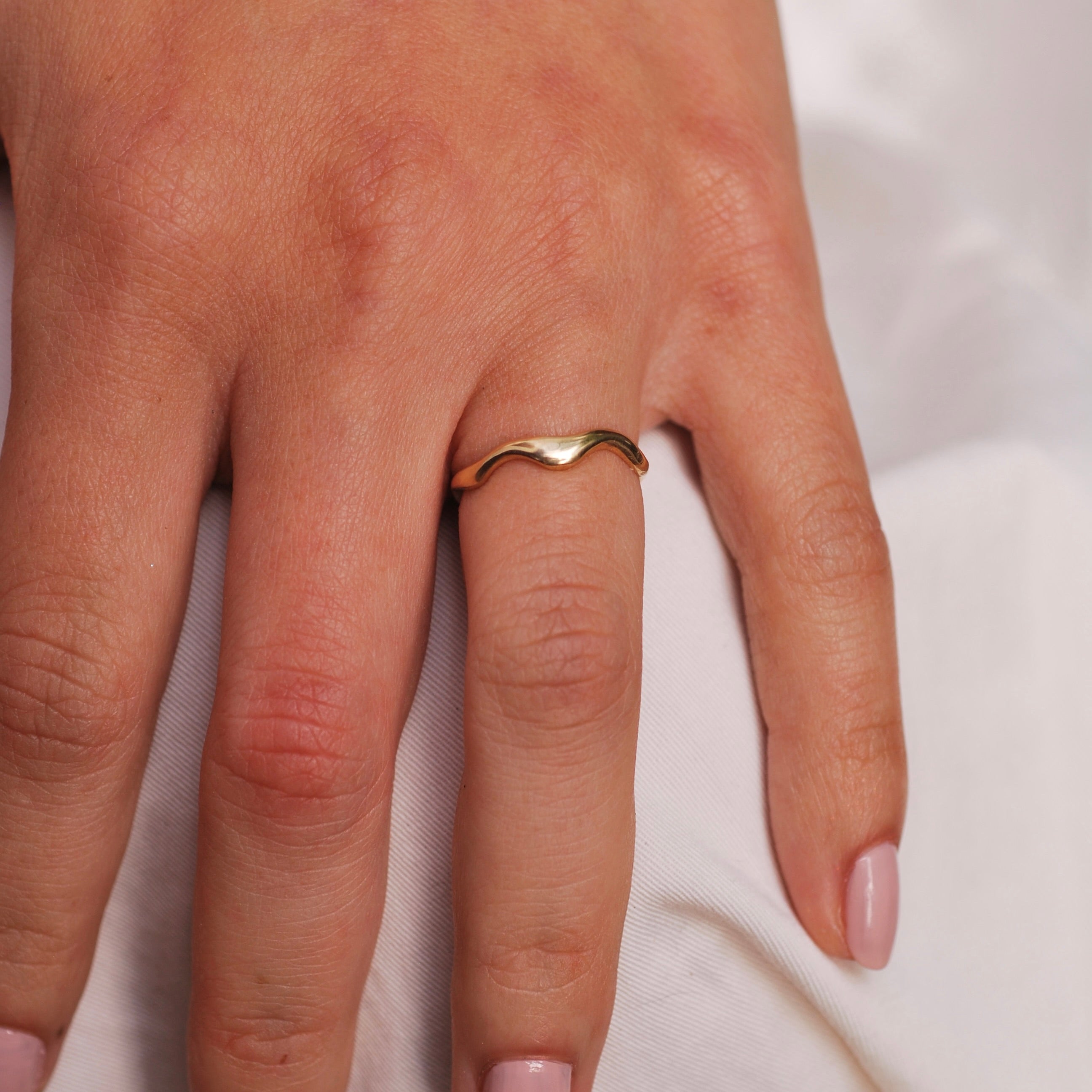 Gold organic wavy ring on a person's finger against a white background
