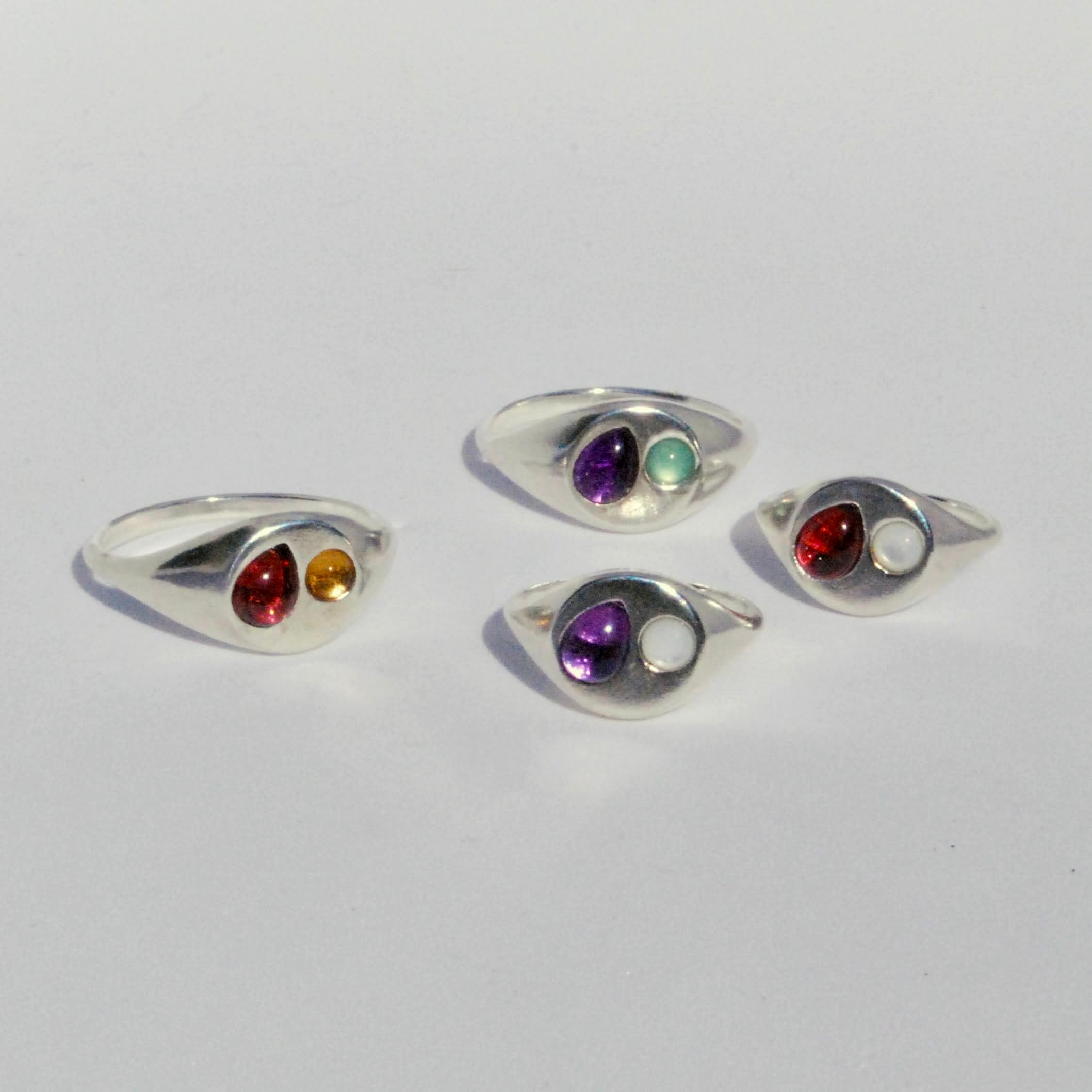 Set of four silver rings with colored gemstones on a light gray background