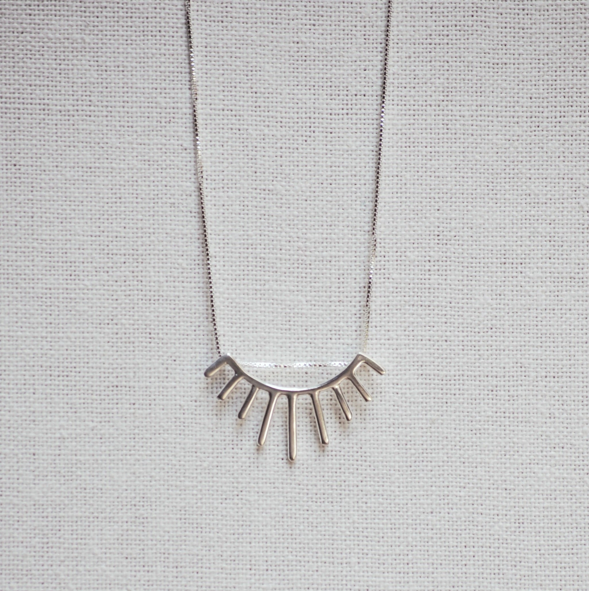 Necklace with eyelash-shaped pendant on a gray textured background