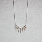 Necklace with eyelash-shaped pendant on a gray textured background