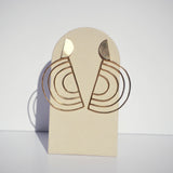 Large bronze rainbow earrings on a tan stand with a white background