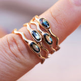 Gold wavy rings with bi-color sapphire gemstones on a finger against a blurred background