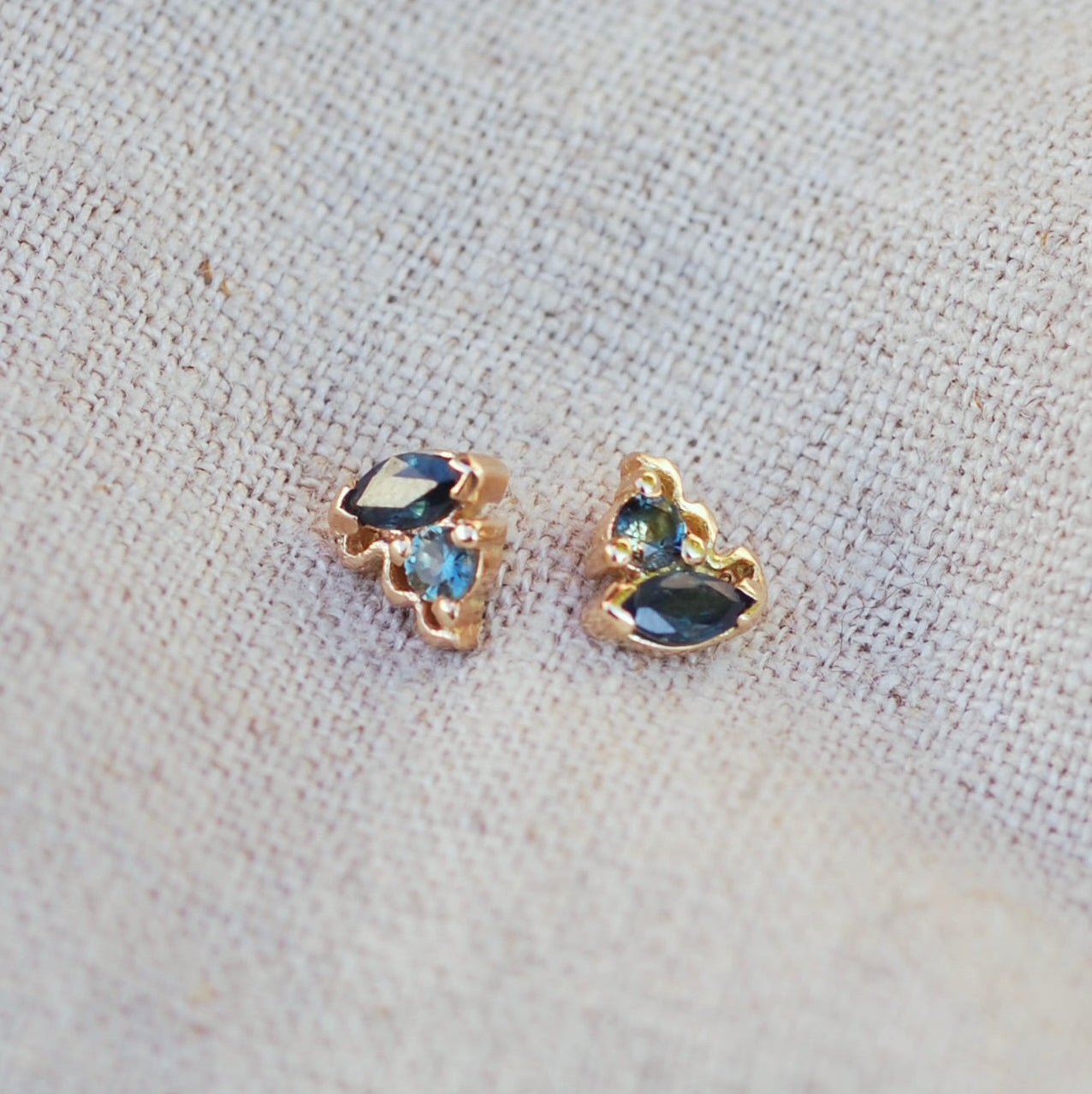 Pair of gold earrings with blue sapphire gemstones on a textured fabric background