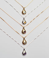 Set of gold and silver teardrop pendants on thin chains against a light gray background