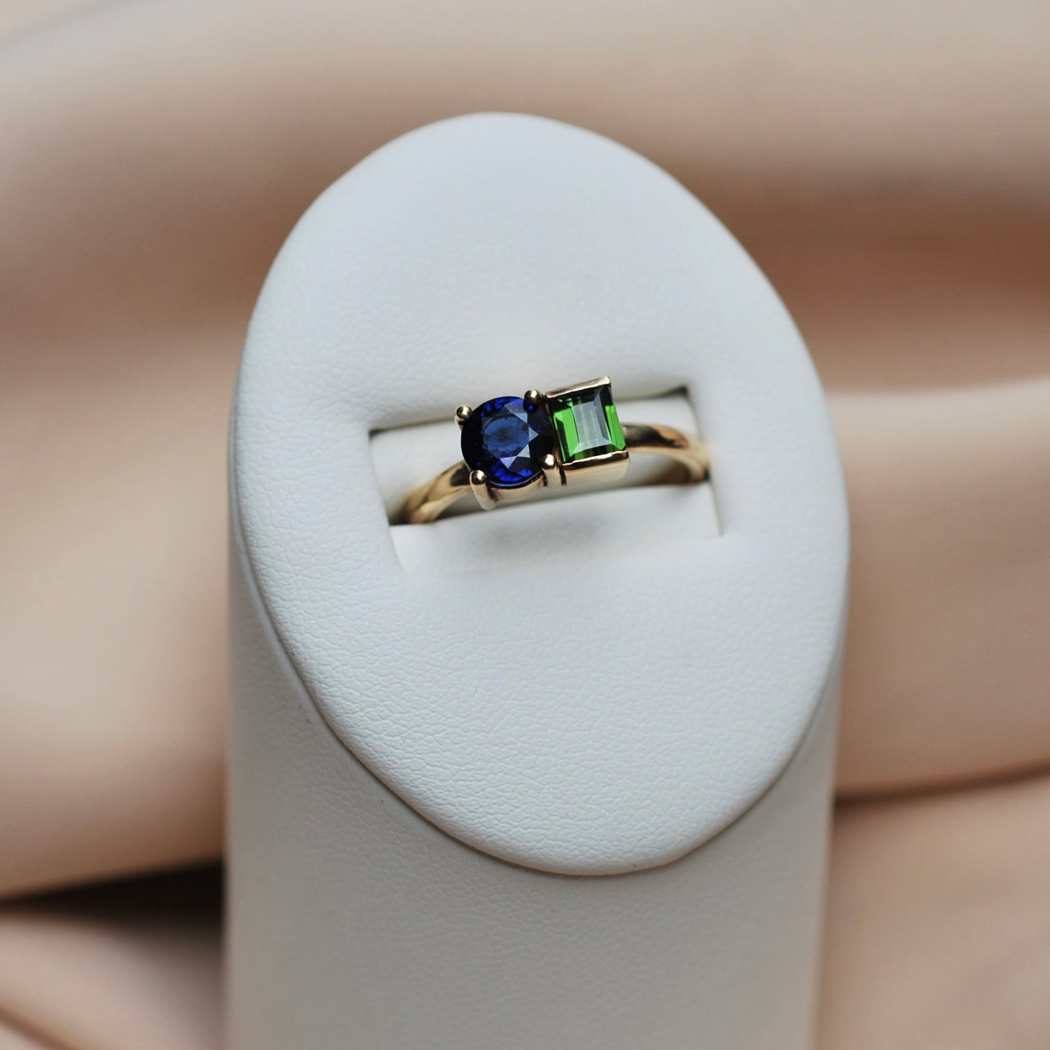 Gold ring with a blue and green gemstone on a white cushion against a beige background