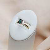 Gold ring with a green and pink gemstone on a white stand against a neutral background
