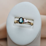 14k yellow gold ring with tourmaline and sapphire gemstones on a white cushion against a beige background