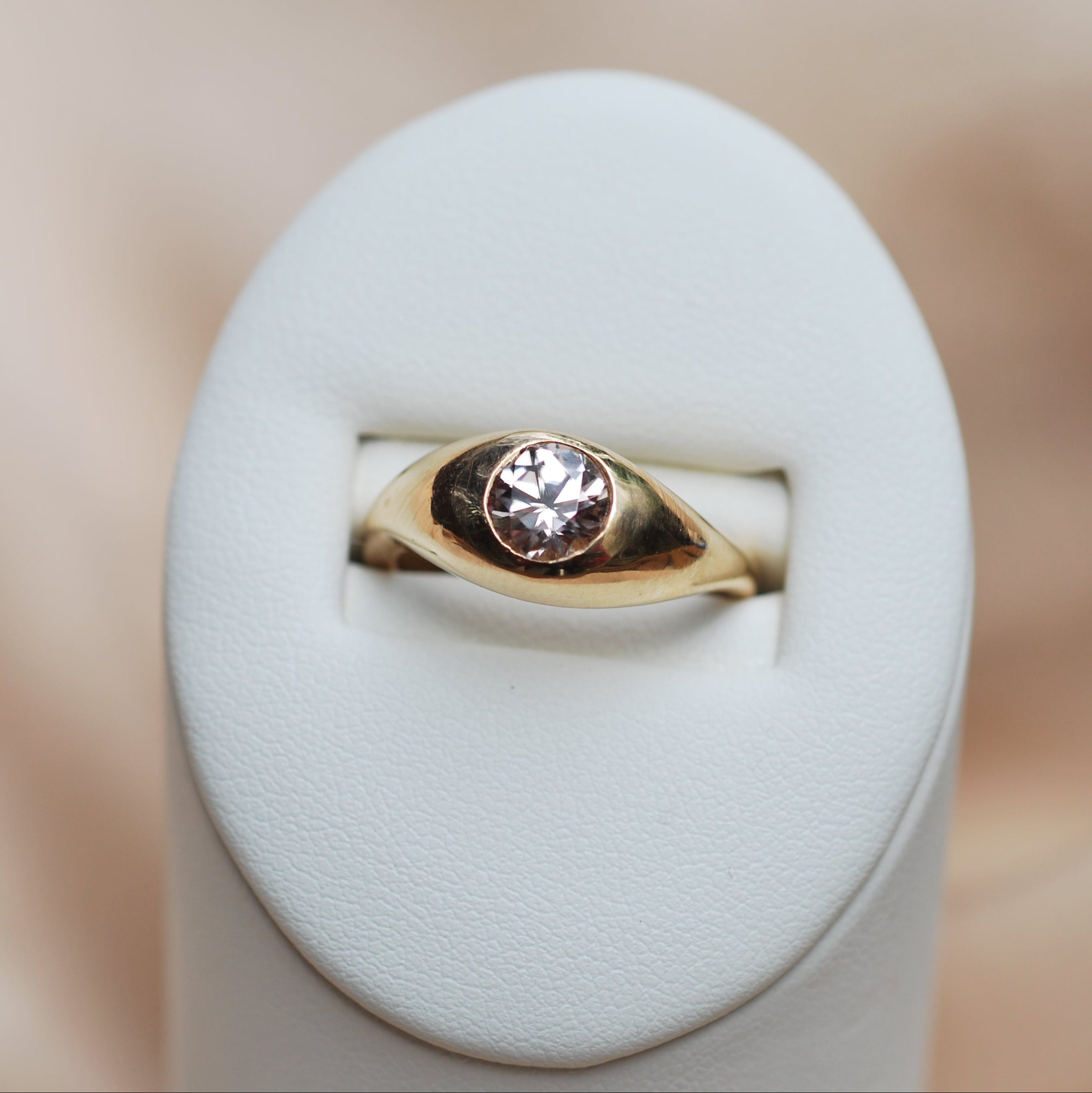 Gold ring with a pink zircon on a white stand against a blurred background