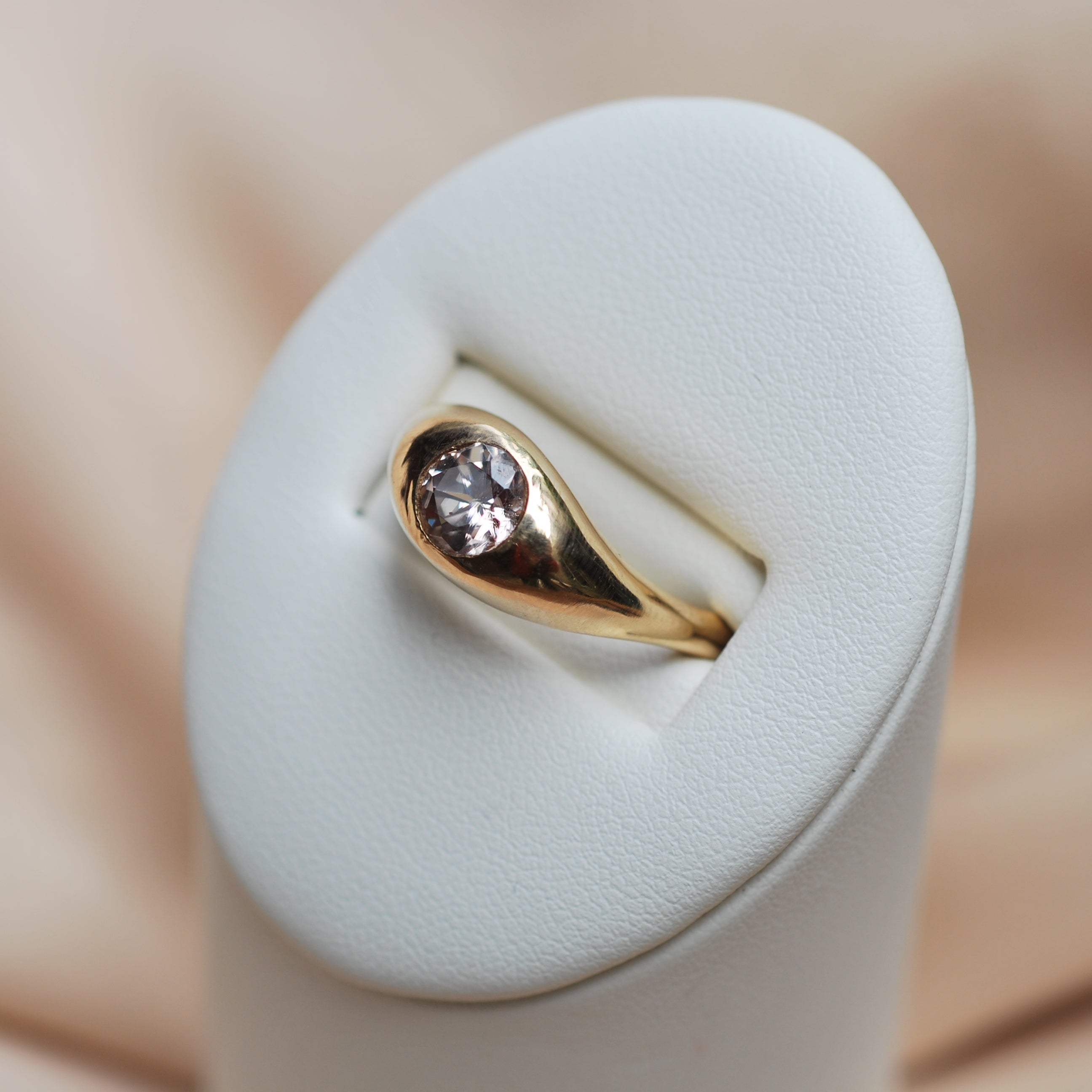 Gold ring with a zircon on a white cushion against a beige background