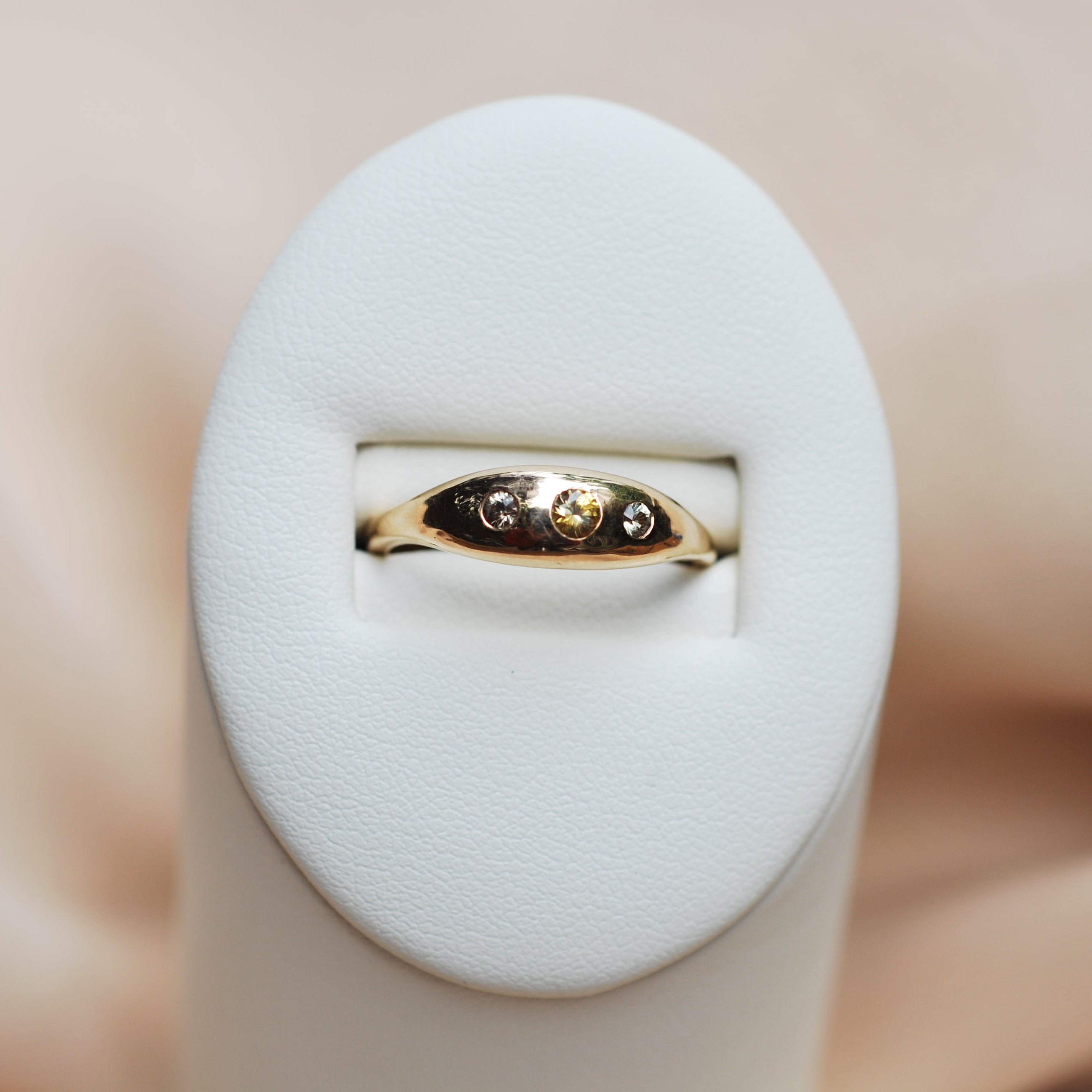 Gold ring with a diamond on a white cushion against a beige background