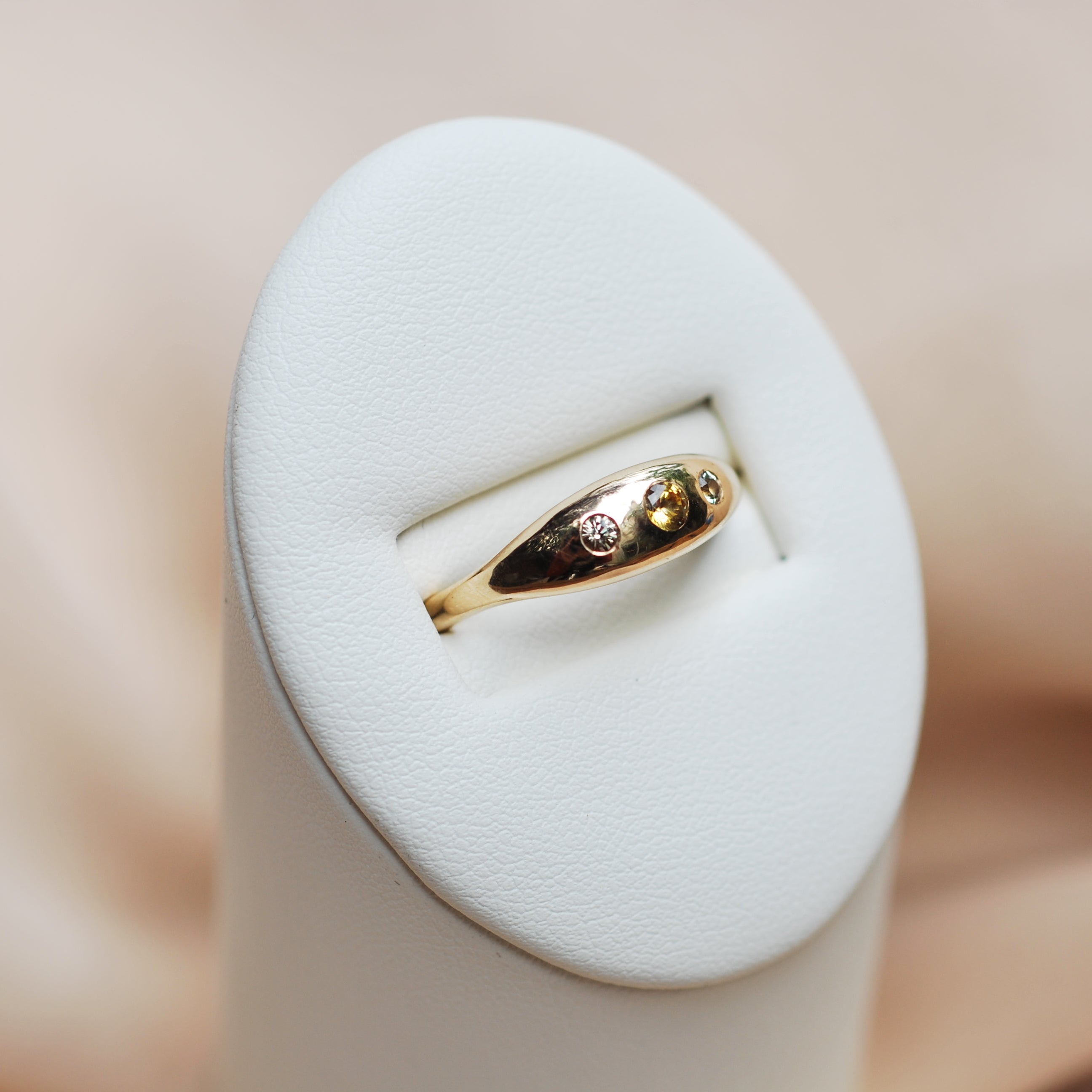 Gold ring with three flush set kaleidoscope sapphires on a white jewelry box with a soft beige background