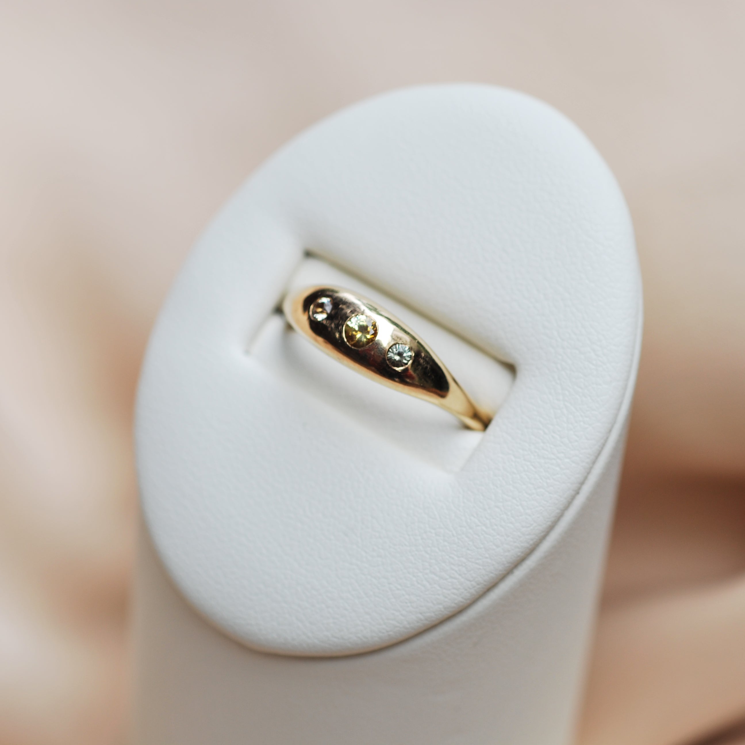 Gold ring with sapphires on a white stand against a soft pink background