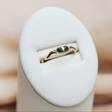 Gold ring with a bi-color sapphire gemstone in a white ring display on a beige background