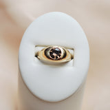 Gold ring with a zircon flush set faceted stone on a white cushion against a beige background