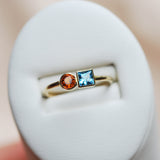 Gold ring with a blue square aquamarine gemstone and a round orange citrine gemstone