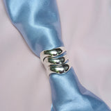 three wide silver organic rings on a blue satin fabric 