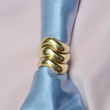 Three bronze wavy organic rings stacked on a satin blue fabric 
