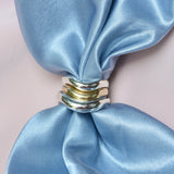 Silver and bronze narrow organic rings on a blue satin fabric