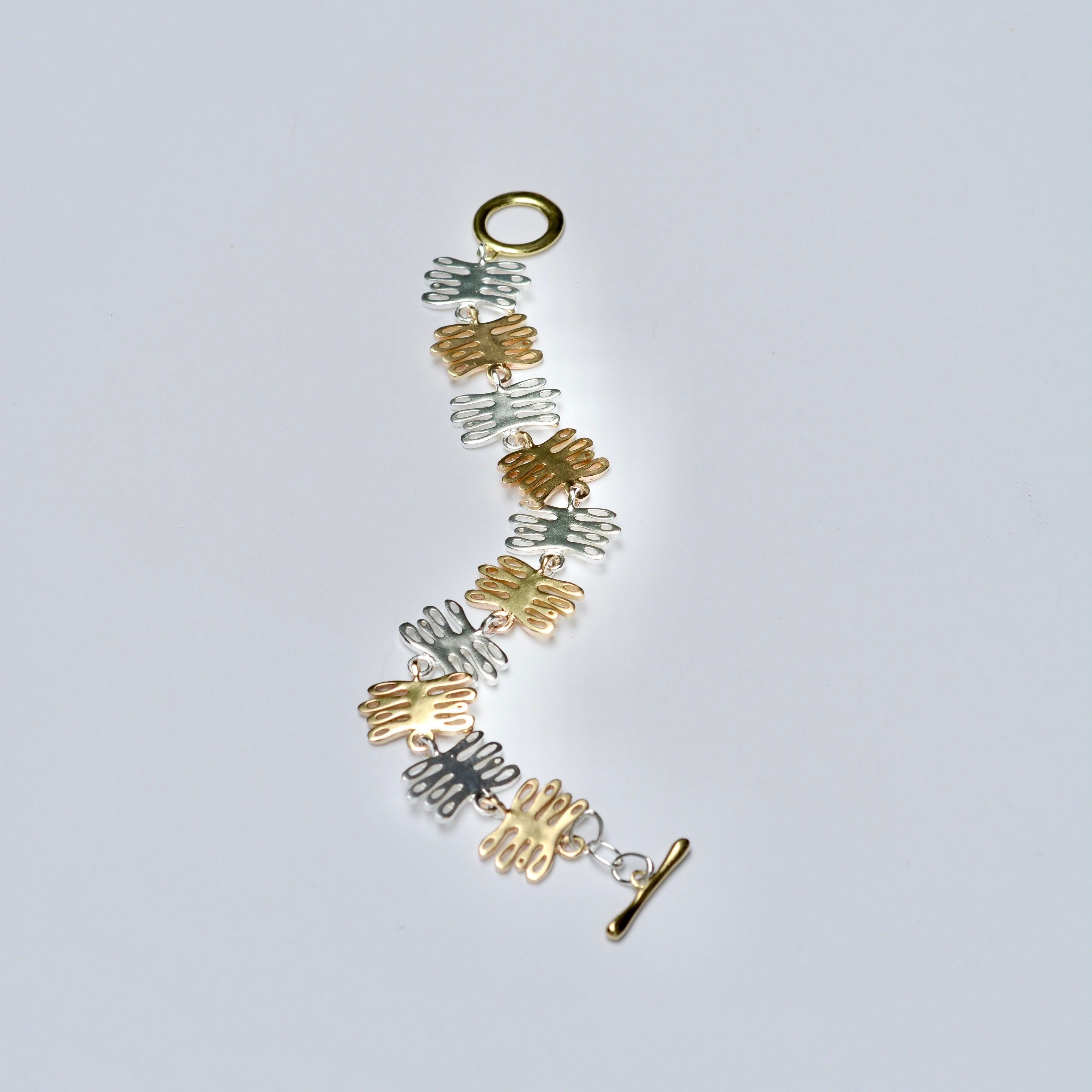 Gold and silver bracelet with coral shaped charms on a light gray background