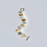 Gold and silver bracelet with coral shaped charms on a light gray background