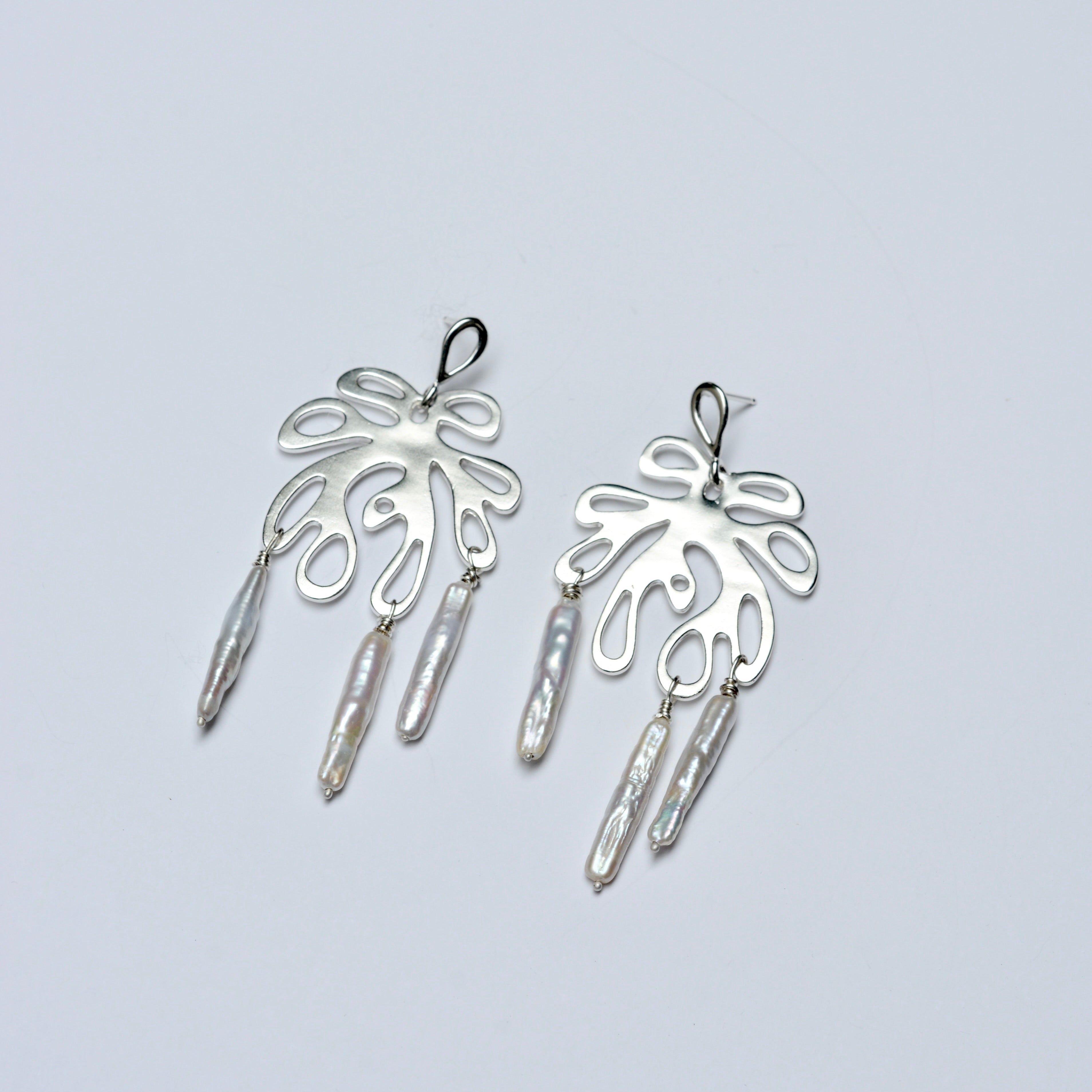 Pair of silver coral earrings with dangling pearls on a light gray background