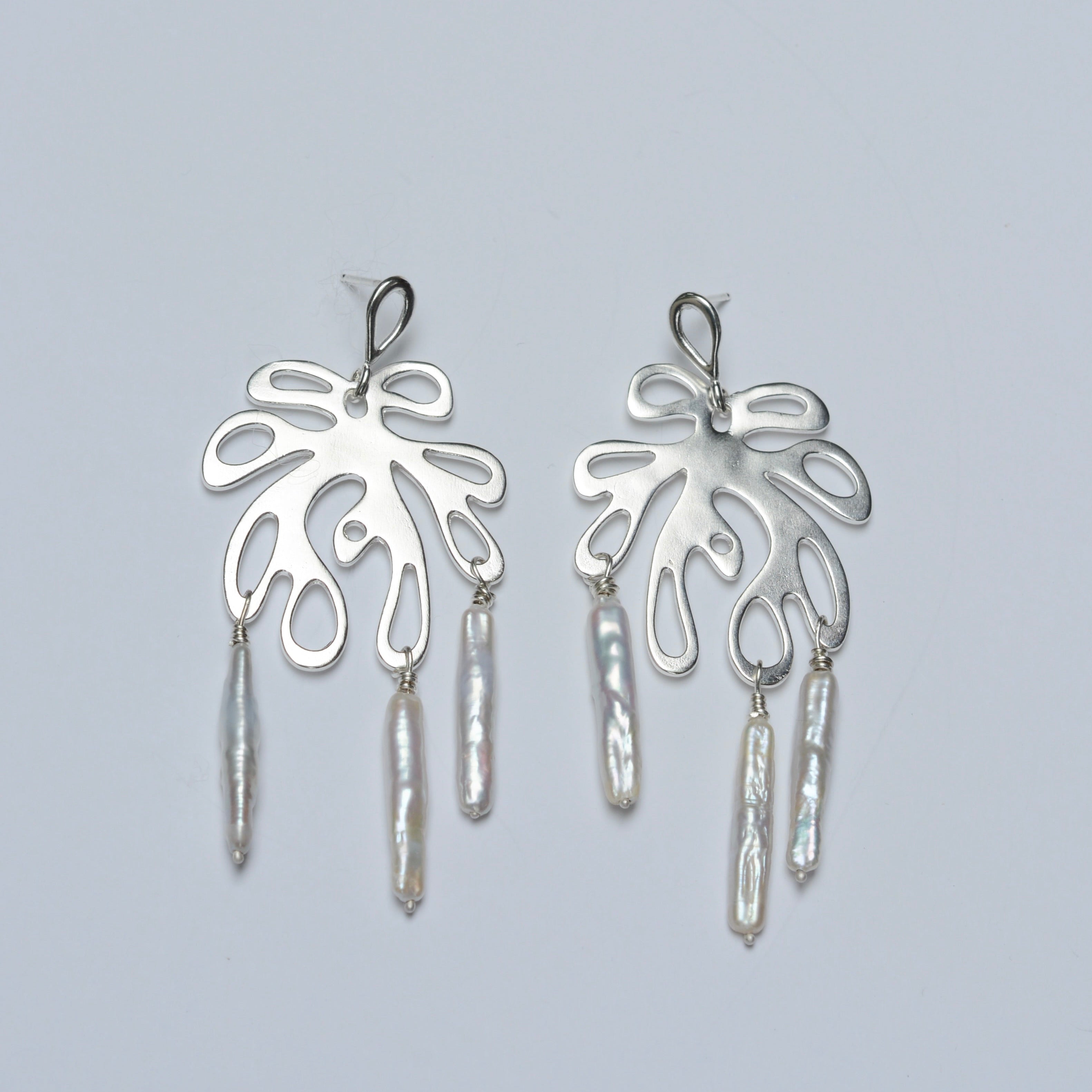 Pair of silver earrings with leaf-like designs and dangling pearls on a light gray background