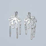 Pair of silver earrings with leaf-like designs and dangling pearls on a light gray background