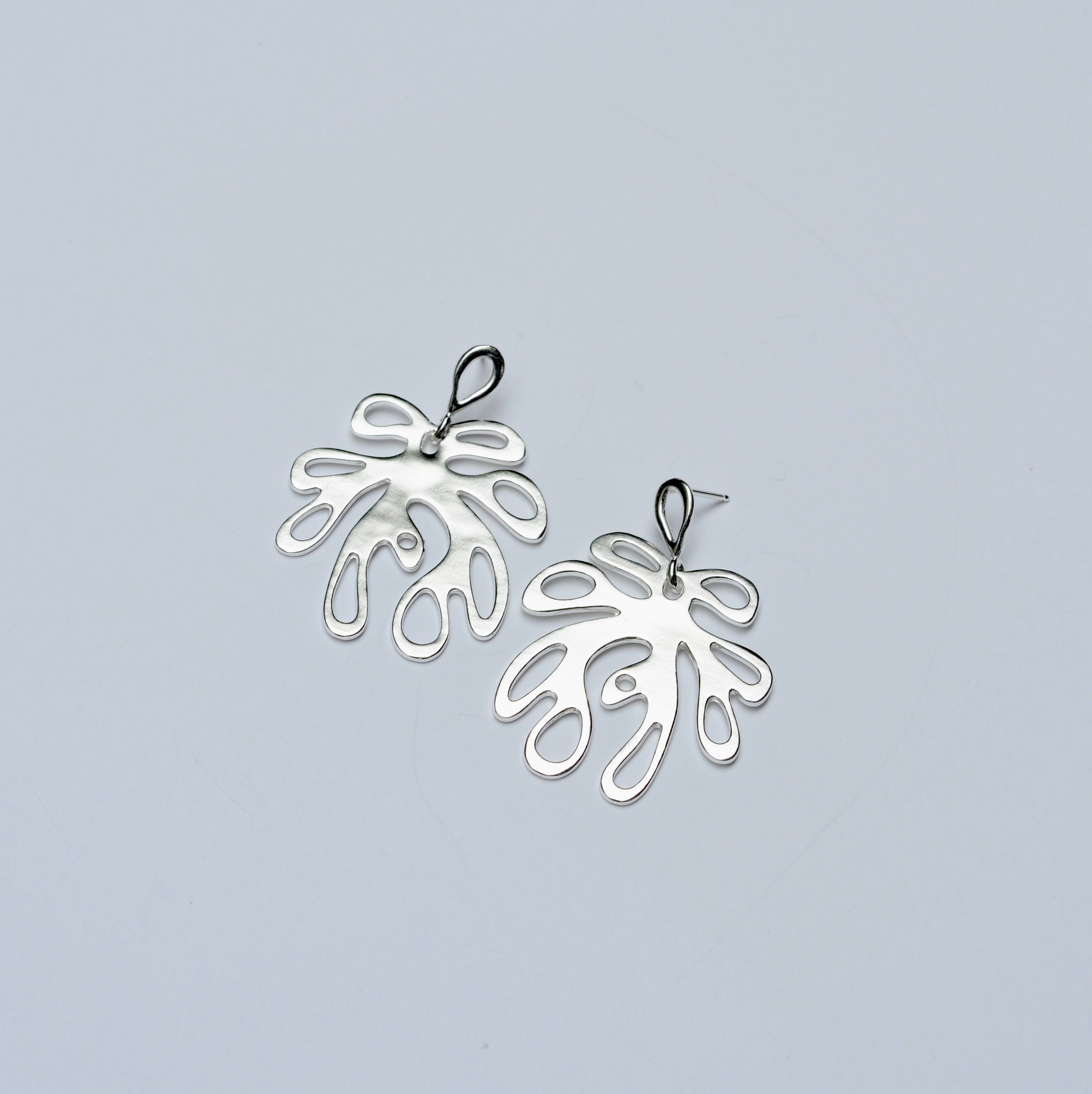 Pair of silver leaf-shaped earrings on a light gray background