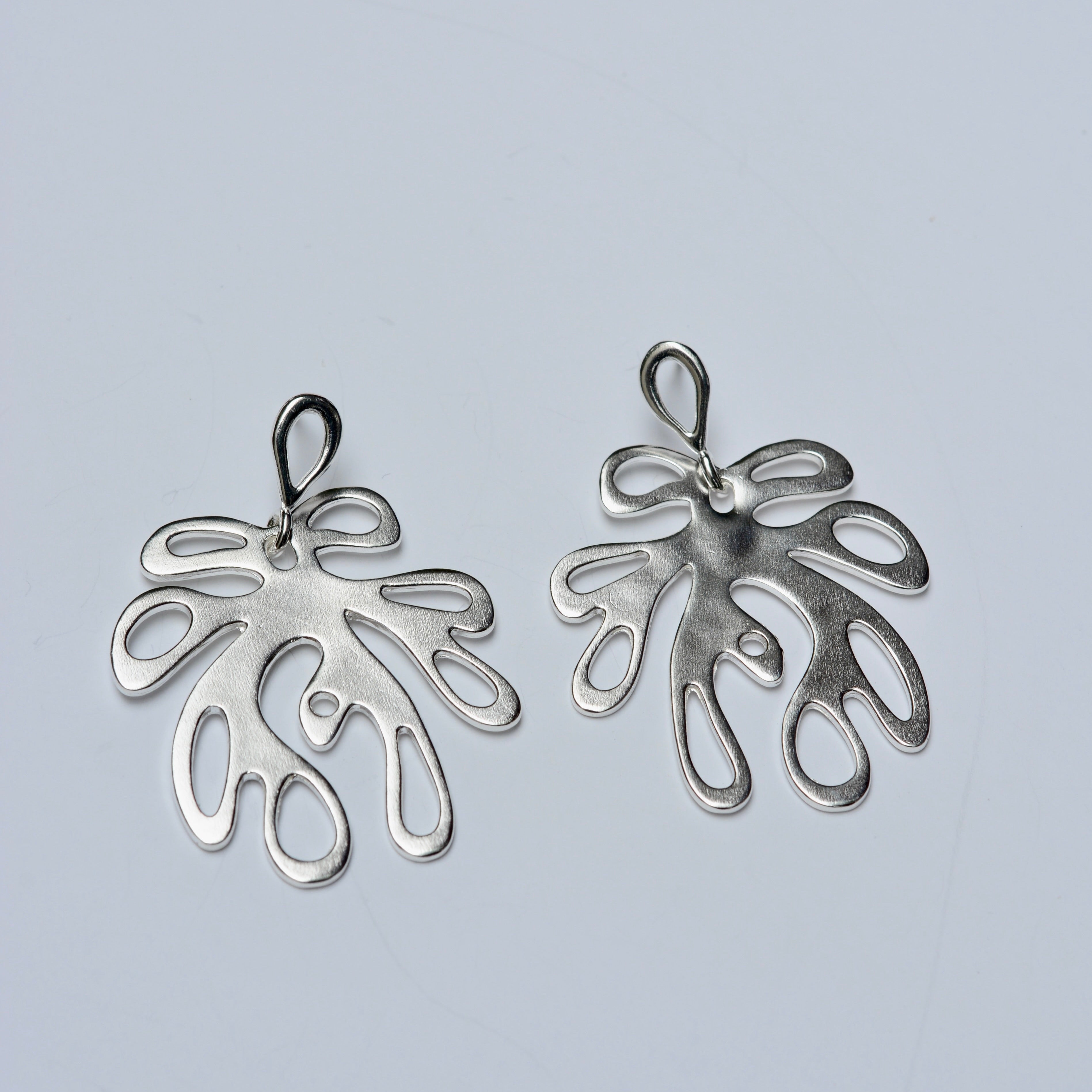 Silver coral shaped earrings on a light gray background