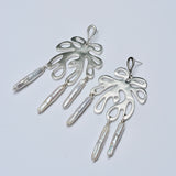 Pair of silver earrings with leaf-like designs and pearls on a light gray background