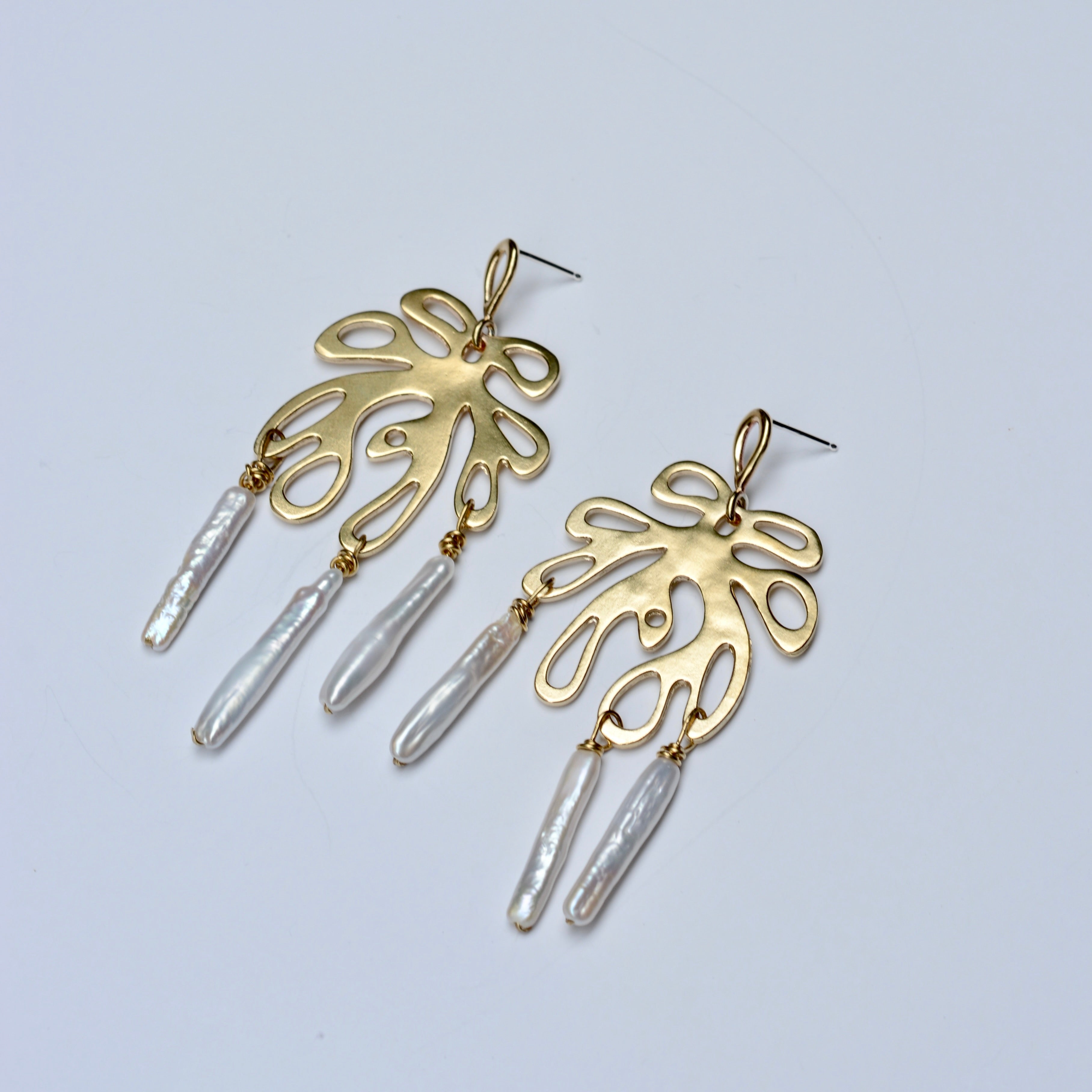Gold coral earrings with pearl drops on a light gray background