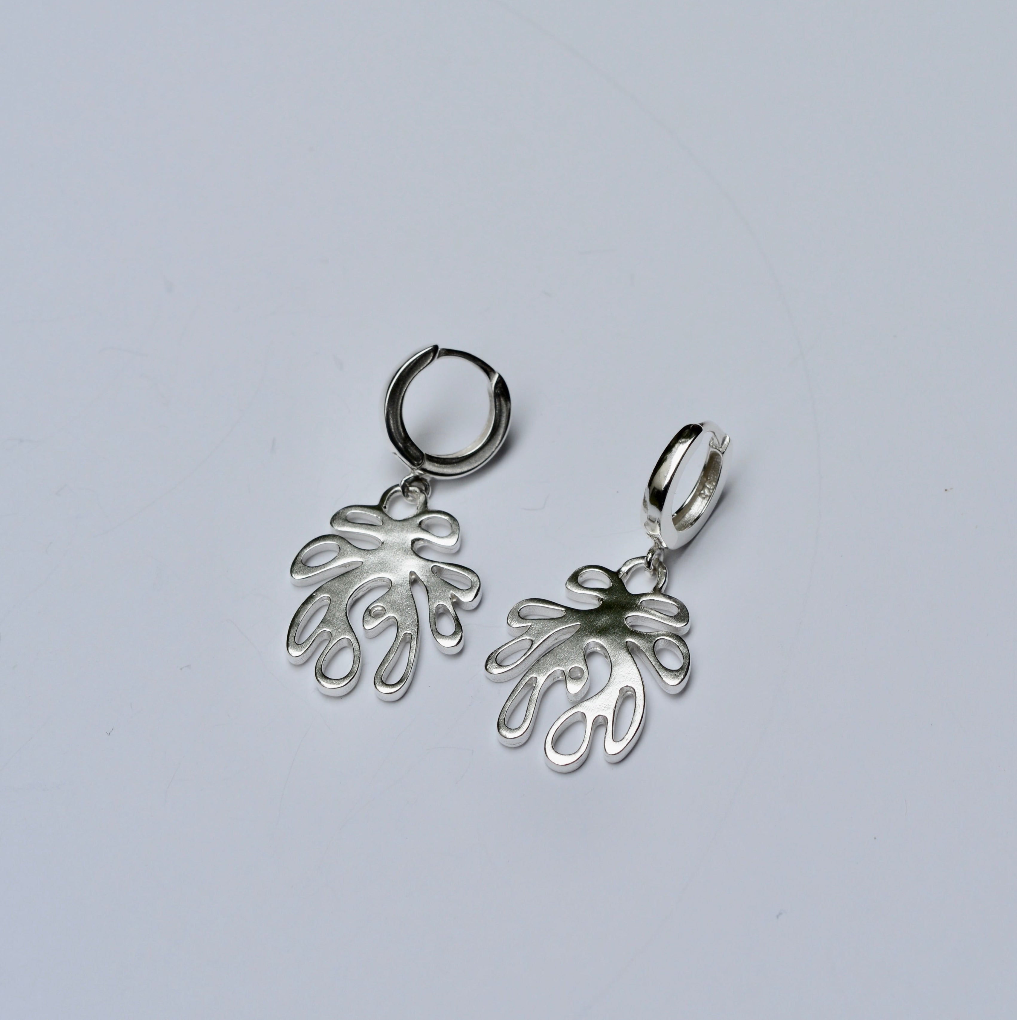 Silver coral shaped earrings with huggie hoops on a grey background