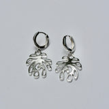 Pair of silver huggie hoop earrings with a coral shaped charm on a light gray background